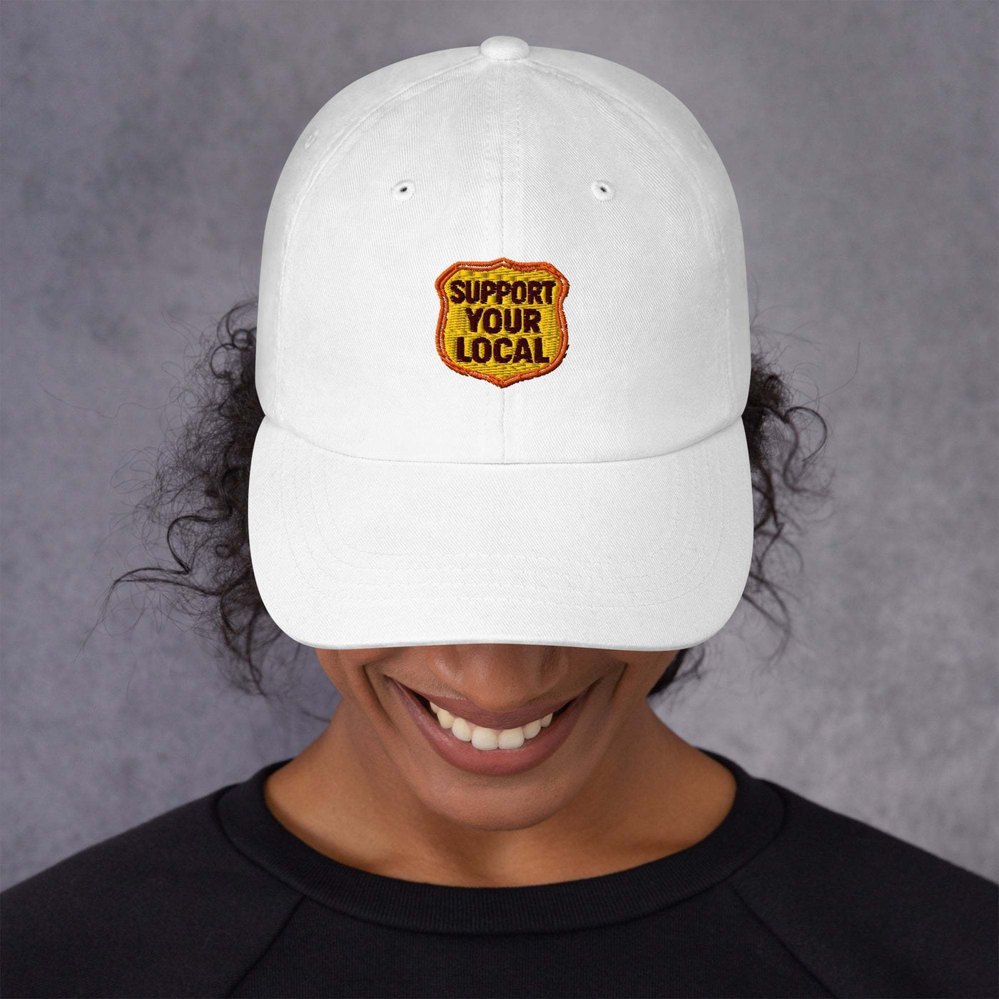 White low-profile dad hat with "Support Your Local" embroidered patch and adjustable strap.
