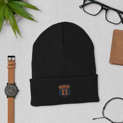 Black cuffed beanie with Texas 11 patch, laid flat with watch, glasses, and wallet on gray surface