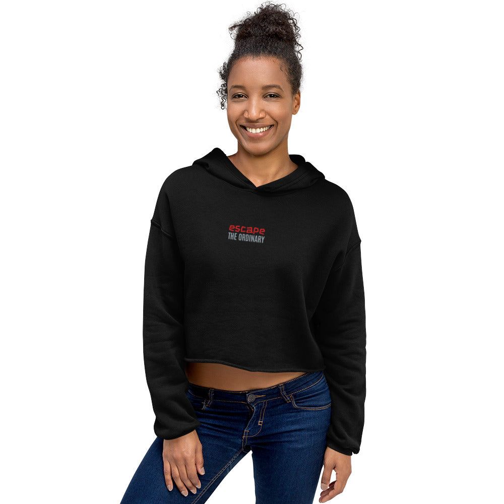 Black crop hoodie with raw hem and red "escape the ordinary" text worn by smiling woman